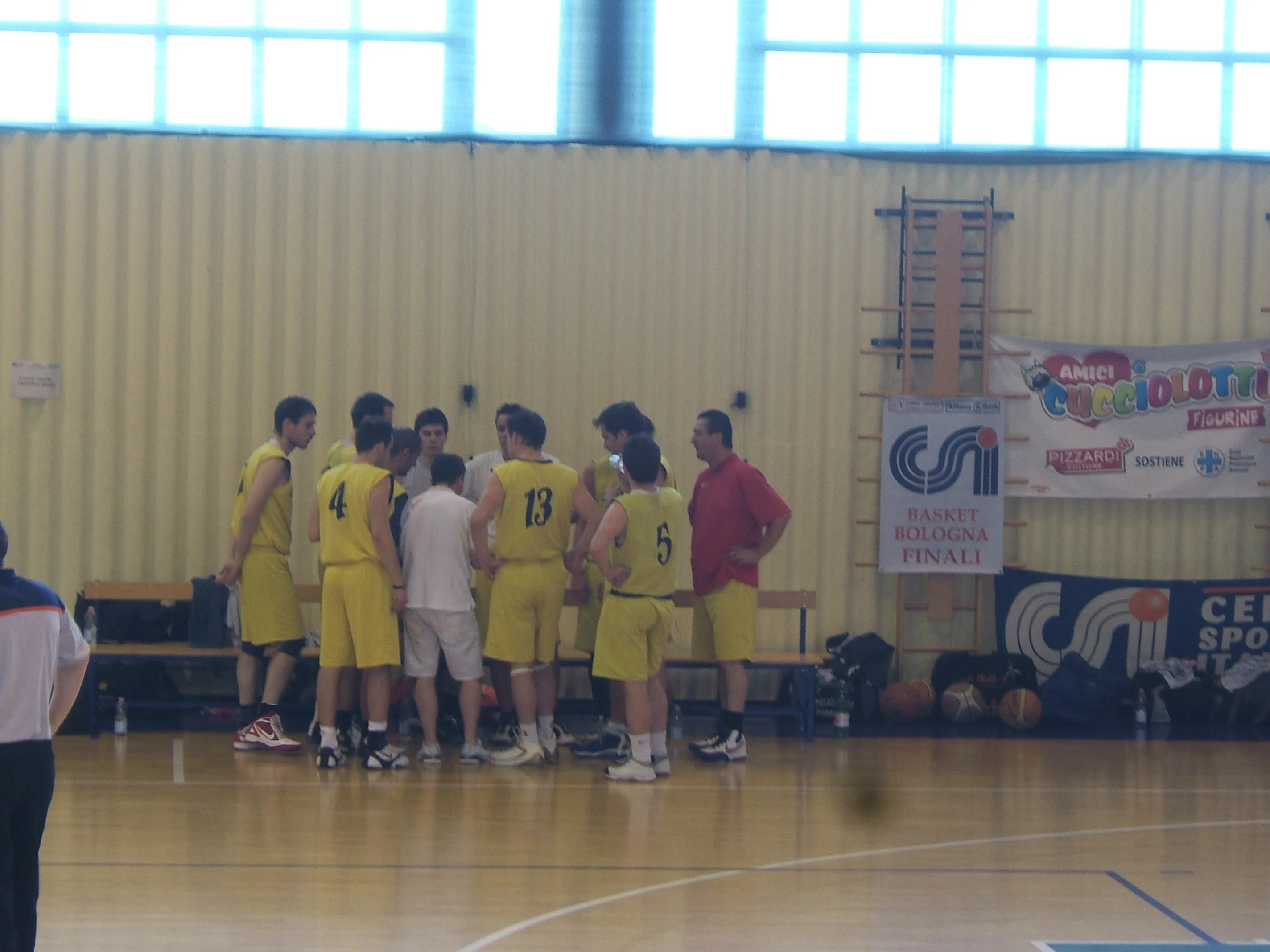 La squadra raccolta attorno all'allenatore durante un time-out, sullo sfondo lo striscione «CSI Basket Bologna Finali»