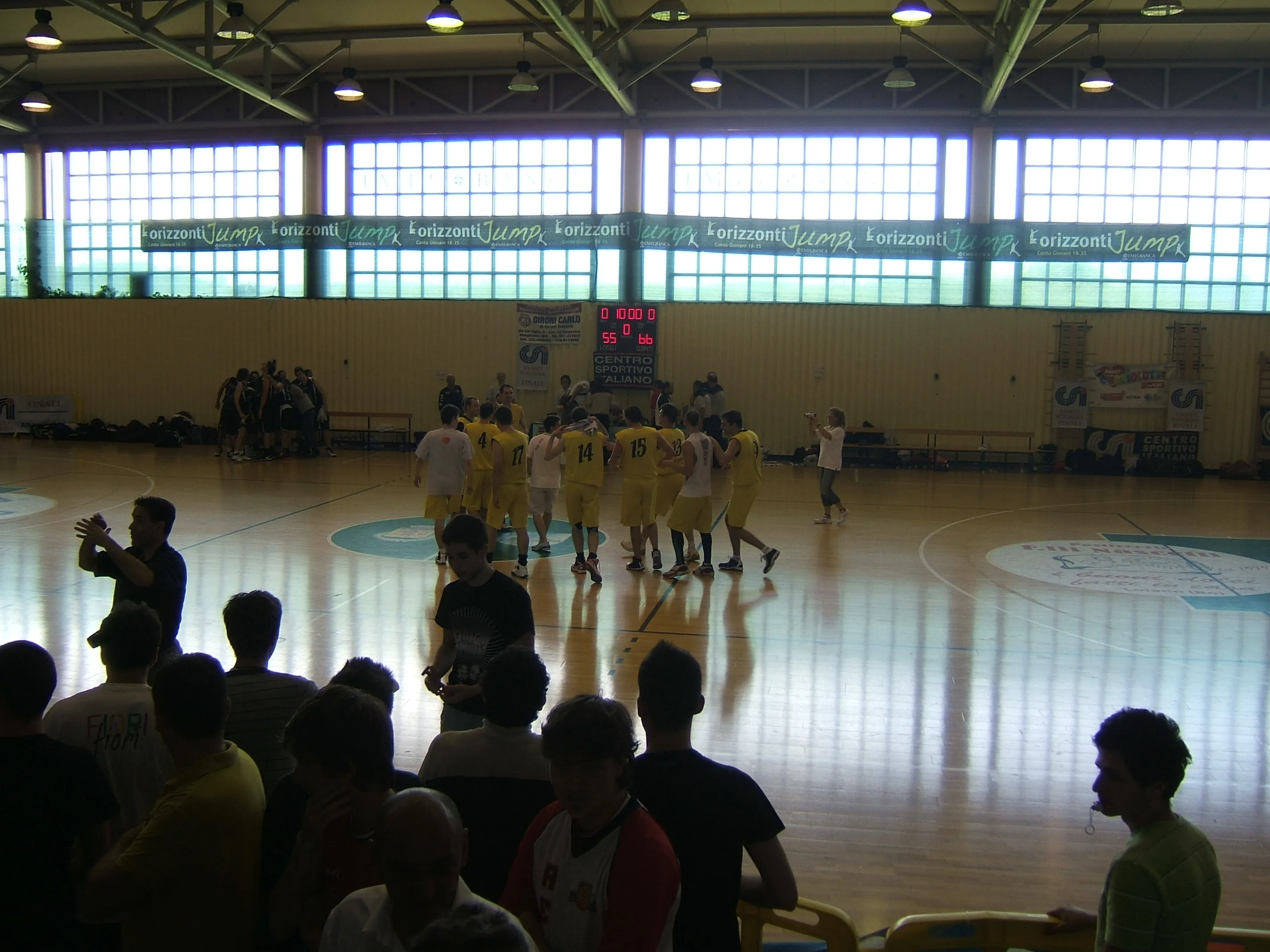 Il tabellone segna 55-66 a fine partita mentre i giocatori in giallo si abbracciano al centro del campo